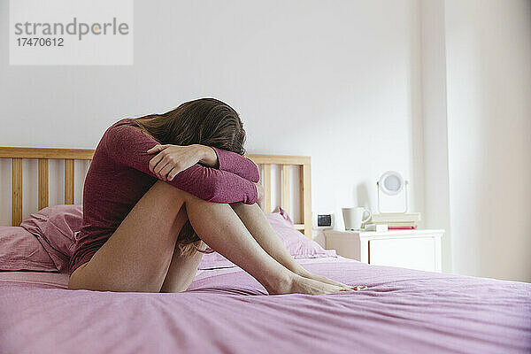 Traurige junge Frau sitzt zu Hause auf einem rosa Bett