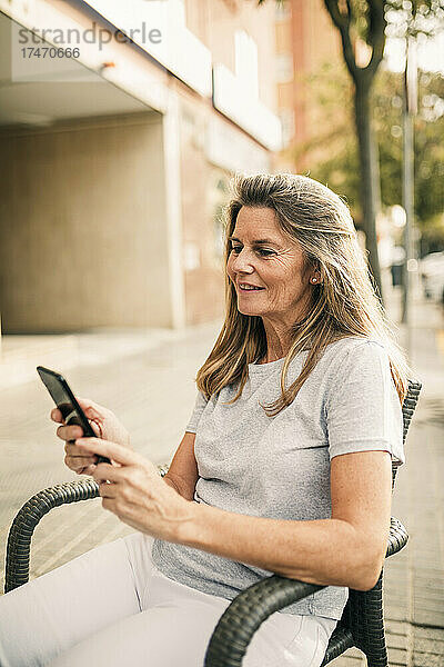 Lächelnde reife Frau  die im Straßencafé mit dem Handy im Internet surft