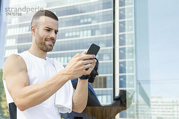 Männlicher Athlet benutzt Smartphone an Glaswand