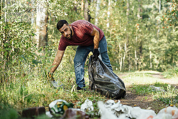 Mittlerer erwachsener männlicher Umweltschützer sammelt Müll im Wald