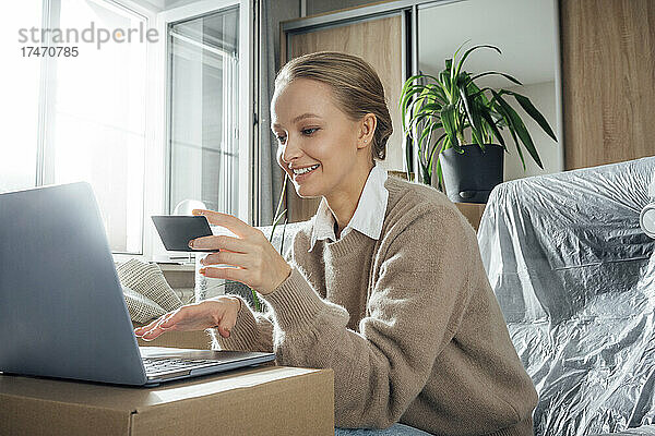 Lächelnde Frau mit Kreditkarte  die zu Hause online per Laptop bezahlt