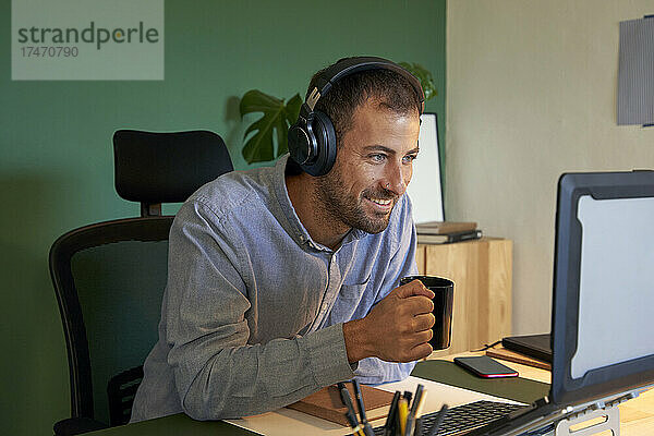 Lächelnder Freiberufler mit Kopfhörern  der über einen Laptop bei einer Videokonferenz spricht
