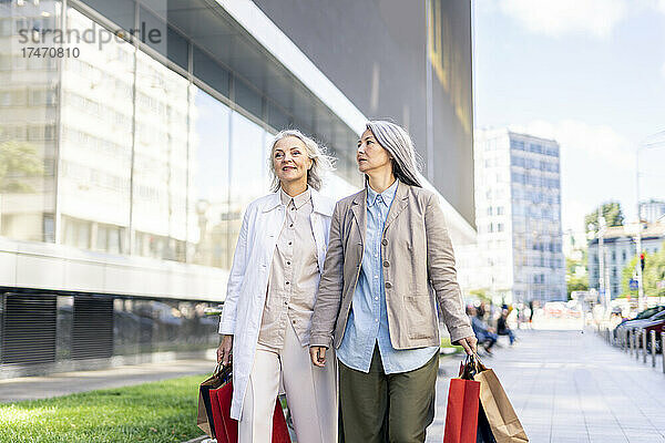 Reife Frauen mit Einkaufstüten gehen auf Fußweg in der Nähe des Einkaufszentrums