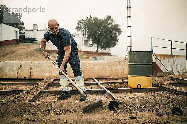 Mann ebnet Boden mit Werkzeug in Kohlefabrik ein