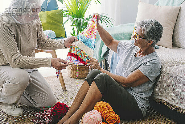 Ältere Frau zeigt Mann im Wohnzimmer gestrickte Wolle