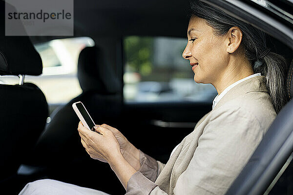 Reife Frau benutzt Mobiltelefon  während sie im Taxi sitzt