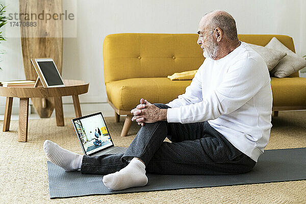 Älterer Mann schaut sich zu Hause Yoga-Tutorial über Laptop an