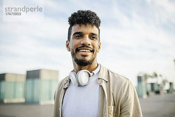 Lächelnder junger Mann mit lockigem Haar und kabellosen Kopfhörern