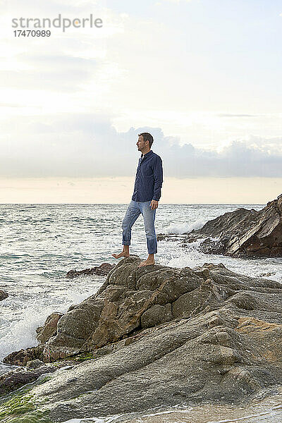 Mann steht bei Sonnenuntergang auf einem Felsen am Meer