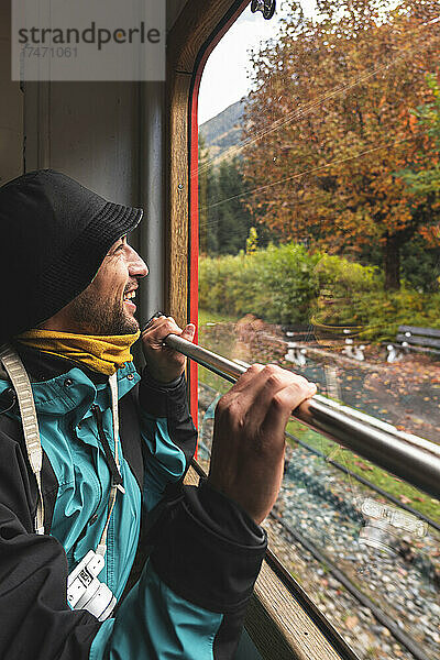 Fröhlicher Mann im Urlaub  der durch das Zugfenster schaut