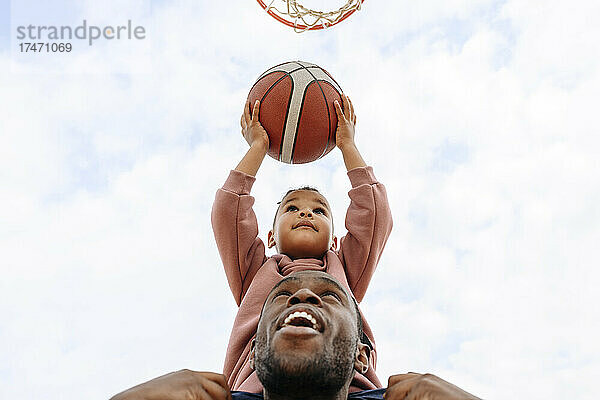 Vater hilft Sohn  Basketball in Korb zu werfen