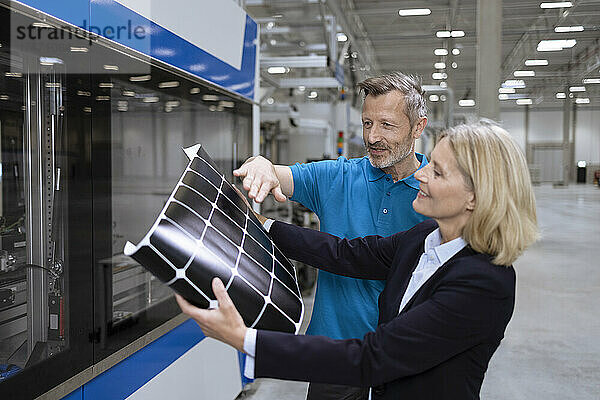 Lächelnde männliche und weibliche Fachkräfte diskutieren über Solarpanel in der Fabrik