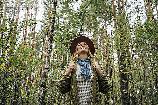 Frau mit Hut schaut nach oben  während sie im Wald steht