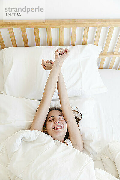 Glückliche Frau dehnt sich beim Aufwachen im Schlafzimmer zu Hause