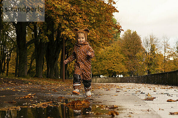 Netter Junge im Regenmantel läuft auf der Straße im Park