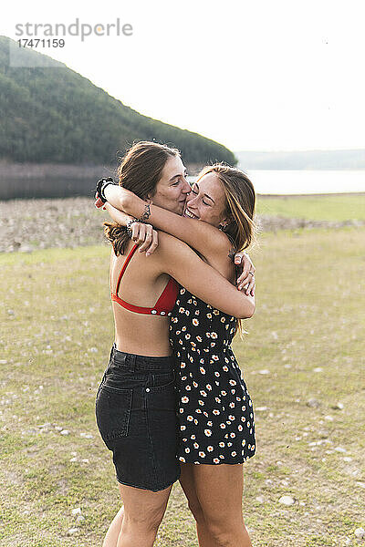 Fröhliche Freundinnen umarmen sich am Seeufer
