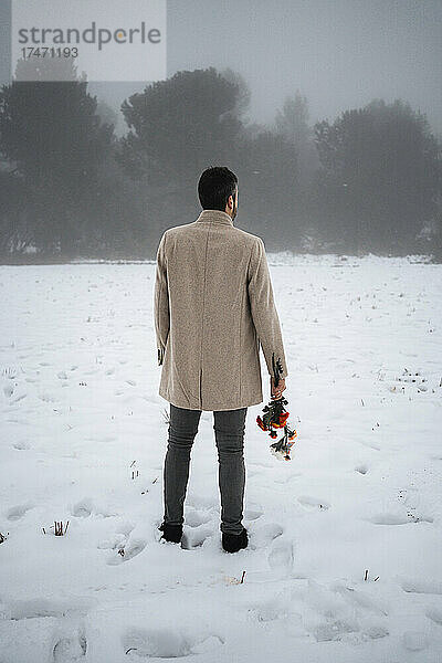 Mann mit Blumen steht im Winter auf Schnee