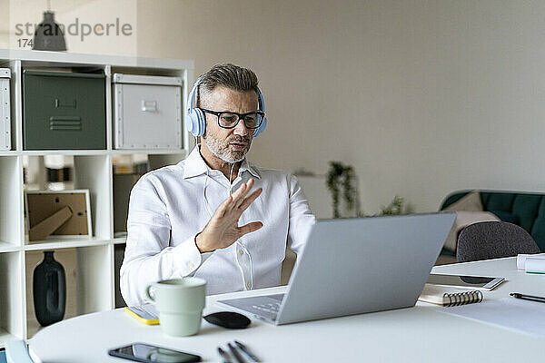 Geschäftsmann winkt bei Videoanruf über Laptop im Büro