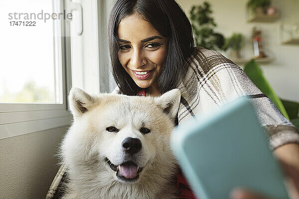 Lächelnde Frau macht zu Hause ein Selfie mit Hund