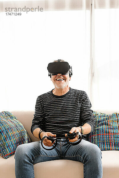 Glücklicher reifer Mann  der zu Hause auf dem Sofa mit einem Virtual-Reality-Simulator spielt