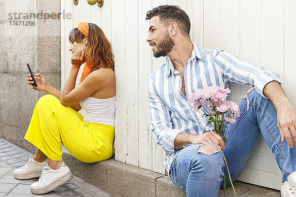 Junger Mann schaut Frau an  die ihr Mobiltelefon benutzt  während sie an der Tür sitzt