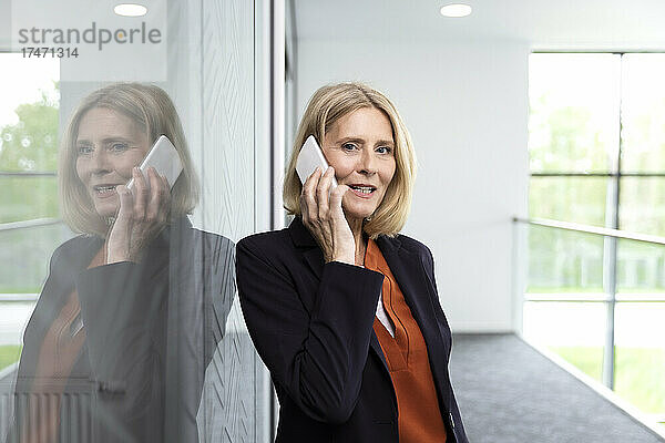 Reife Geschäftsfrau telefoniert im Flur mit Smartphone und Glas