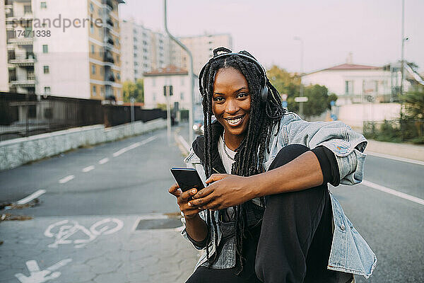 Lächelnde Frau mit Mobiltelefon  die auf dem Fußweg Musik hört