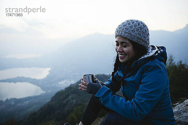 Lächelnde Frau mit geschlossenen Augen hält Kaffeetasse auf dem Berg