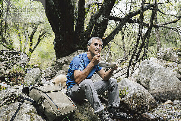 Reifer männlicher Tourist isst Essen  während er auf einem Felsen sitzt