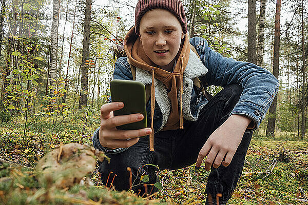 Junge kniet im Wald und fotografiert mit Smartphone