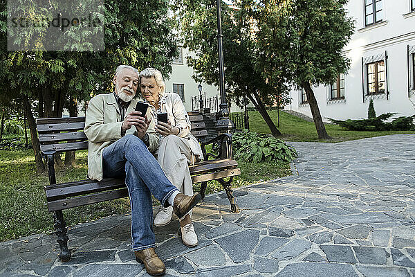 Paar nutzt gemeinsames Smartphone  während es auf Bank sitzt