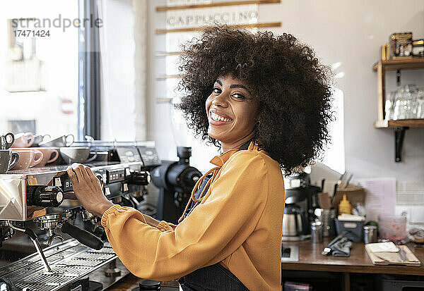 Lächelnde Kellnerin mit Afro-Frisur steht an der Kaffeemaschine