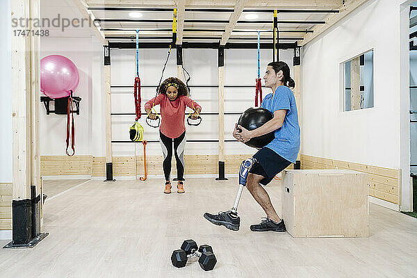 Behinderter Sportler hält Medizinball mit Freund beim Training im Fitnessstudio