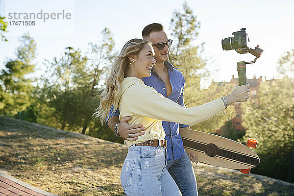 Lächelnde Frau vloggt mit Mann vor der Kamera im Park