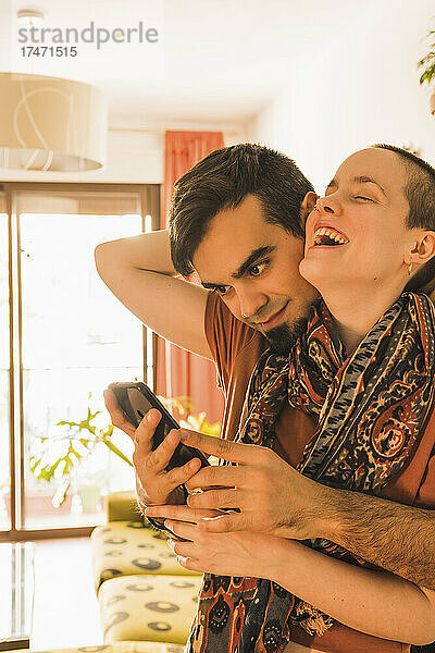 Mann benutzt Mobiltelefon  während er Frau zu Hause umarmt