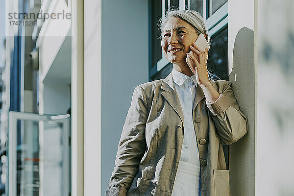 Frau lächelt  während sie vor dem Café mit dem Smartphone spricht