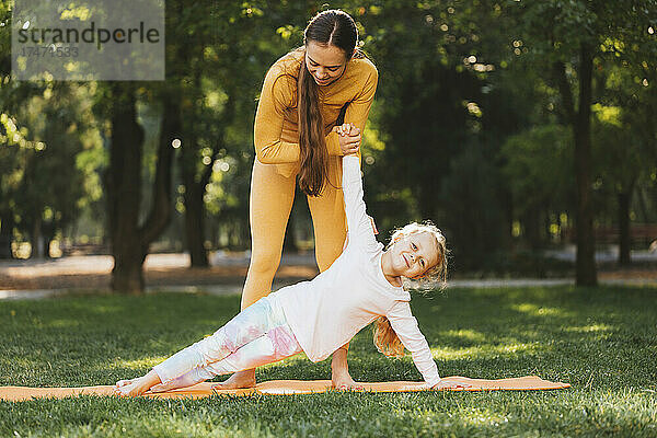 Mutter hilft Tochter beim Yoga im Park