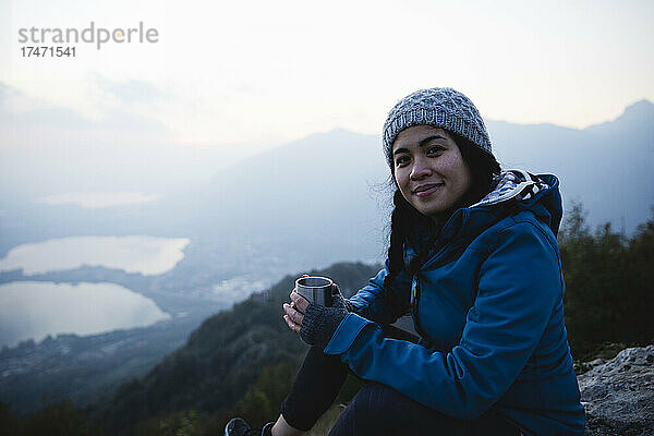 Lächelnder Wanderer mit Kaffeetasse sitzt auf dem Berg