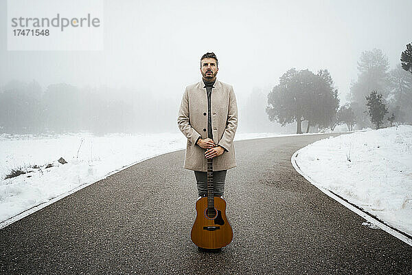 Mann mit Gitarre steht im Winter auf der Straße