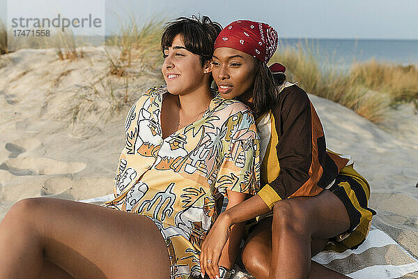 Lesbisches Paar sitzt an einem sonnigen Tag am Strand