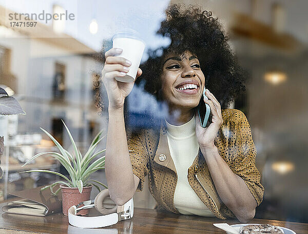 Lächelnde Frau trinkt Kaffee und telefoniert im Café