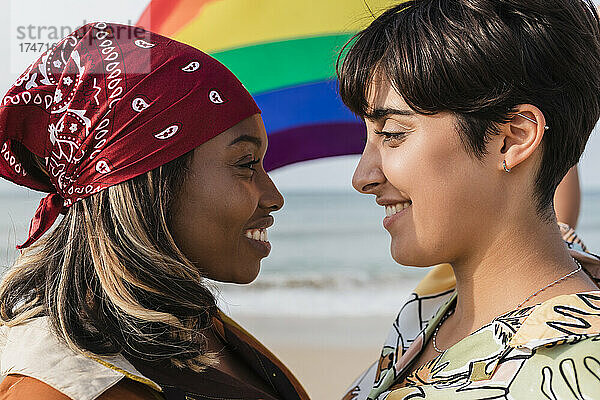 Romantisches lesbisches Paar mit Regenbogenfahne  das sich am Strand anstarrt