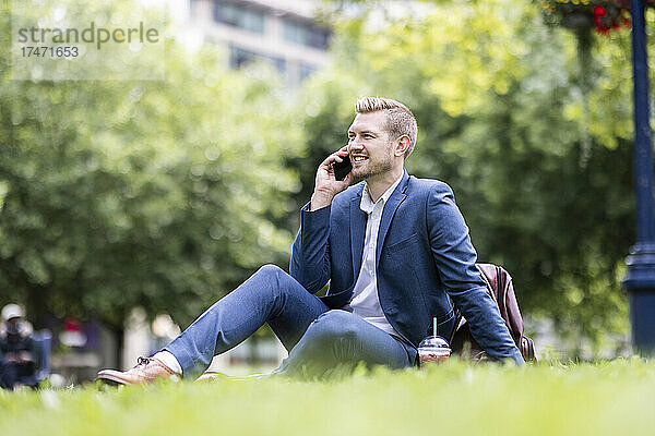 Lächelnder männlicher Profi  der im Park mit dem Smartphone spricht