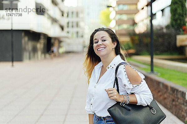 Lächelnde Geschäftsfrau mit Tasche auf Fußweg