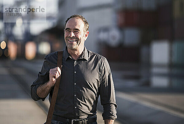Lächelnder Geschäftsmann mit Umhängetasche  der auf der Straße läuft