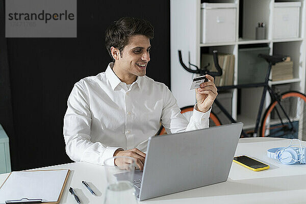 Lächelnder Geschäftsmann beim Online-Einkauf per Laptop im Büro