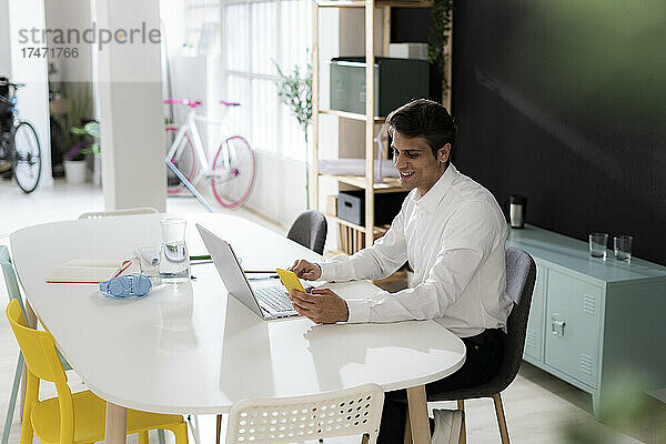 Junger Geschäftsmann mit Smartphone arbeitet am Laptop am Schreibtisch im Büro