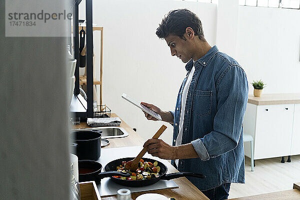 Mann nutzt digitales Tablet beim Zubereiten von Speisen in der Küche