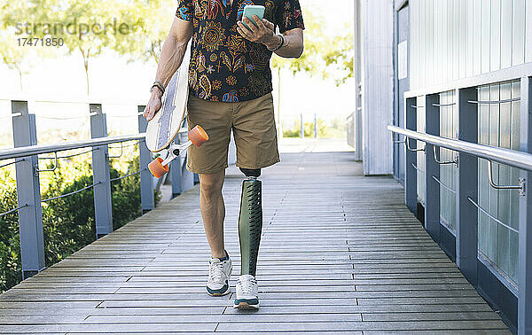 Mann mit Beinprothese benutzt Mobiltelefon auf der Promenade