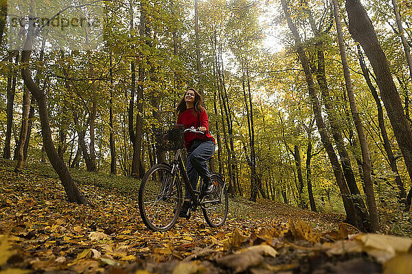 Frau radelt vor Bäumen im Herbstpark